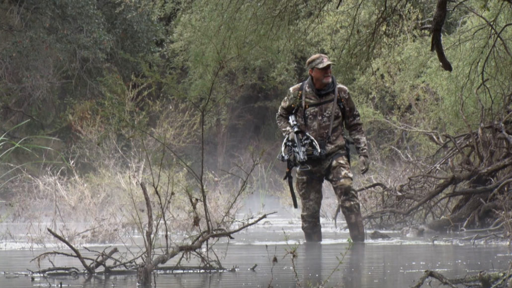 Hunter wading through water with crossbow